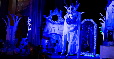 Na zdjęciu kadr z przedstawienia, biała postać z nieproporcjonalnie dużą maską - Królowa Śniegu