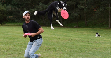 Na zdjęciu mężczyzna, który właśnie rzucił dysk, w powietrzu pies, który własnie go złapał