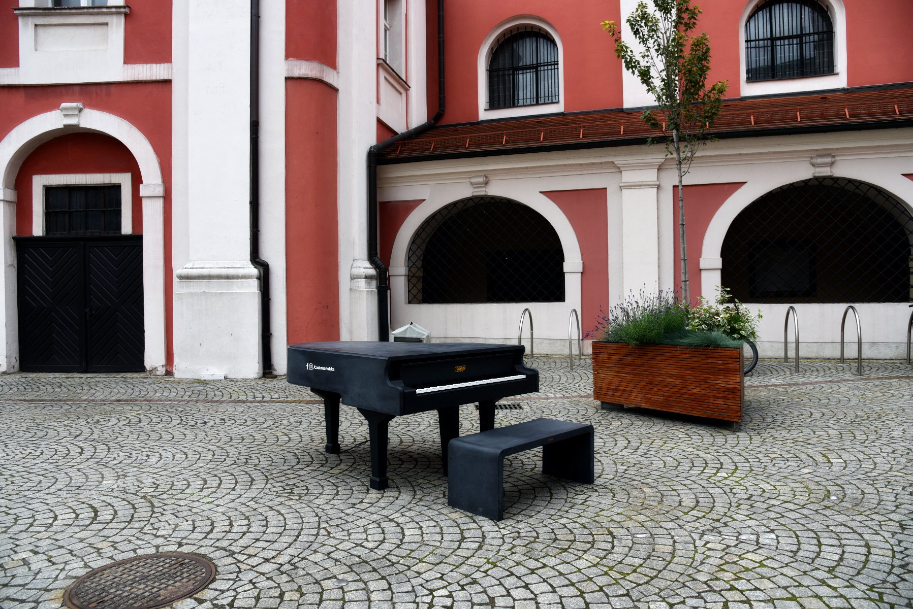Galeria zdjęć przedstawiająca czarny fortepian ustawiony na dziedzińcu urzędu miasta, w tle budynki kolegiaty - grafika artykułu