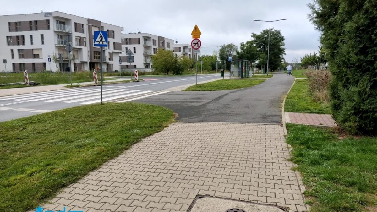 Na pierwszym planie droga rowerowa, w tle wiata przystankowa i zabudowania. - grafika artykułu