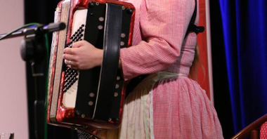 Na zdjęciu kobieta w ludoiwym stroju grająca na akordeonie