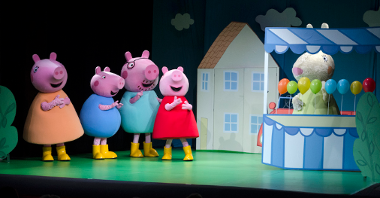 Na scenie znajdują się świnka Peppa oraz 3 inne postaci świnek, z boku znajduje się królik za straganem