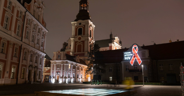 Na zdjęciu plac Kolegiacki, na jednym z budynków wyświetlona czerwona wstążeczka i napis: razem przeciw HIV