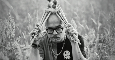 Czarno białe zdjęcie, mężczyzna w okularach, trzymający w dłoniach pałeczki perkusyjne