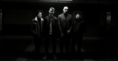 Czarno-białe zdjęcie czterech mężczyzn stojących i patrzących w obiektyw