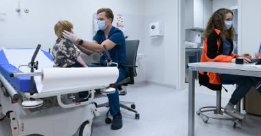 Zdjęcie przedstawia SOR w szpitalu na Wrzoska. Lekarz bada głowę dziecka. Przy biurku obok siedzi ratownik medyczny.