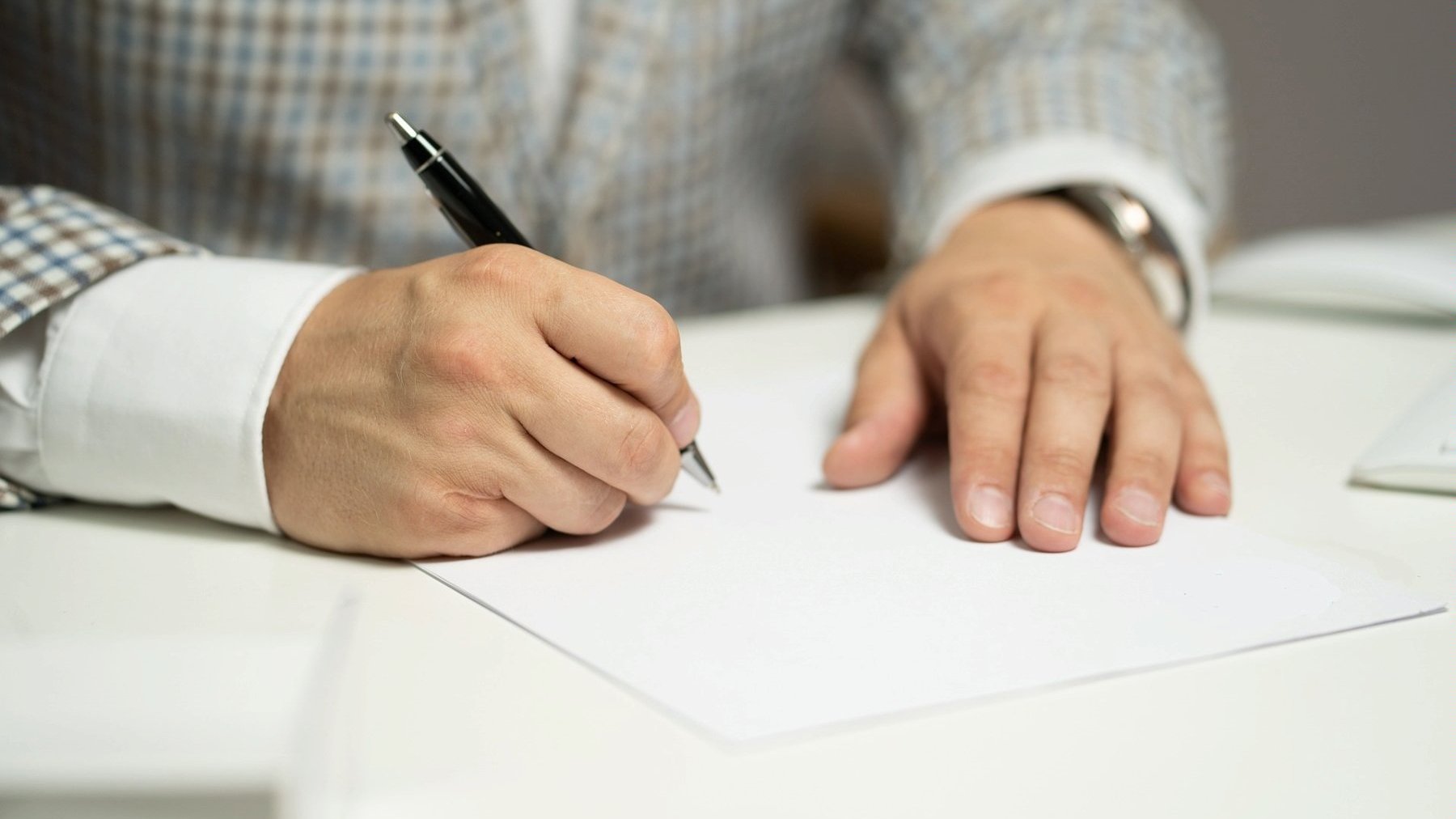 Na zdjęciu dłonie starszej osoby podpisujące coś na karce papieru - grafika artykułu