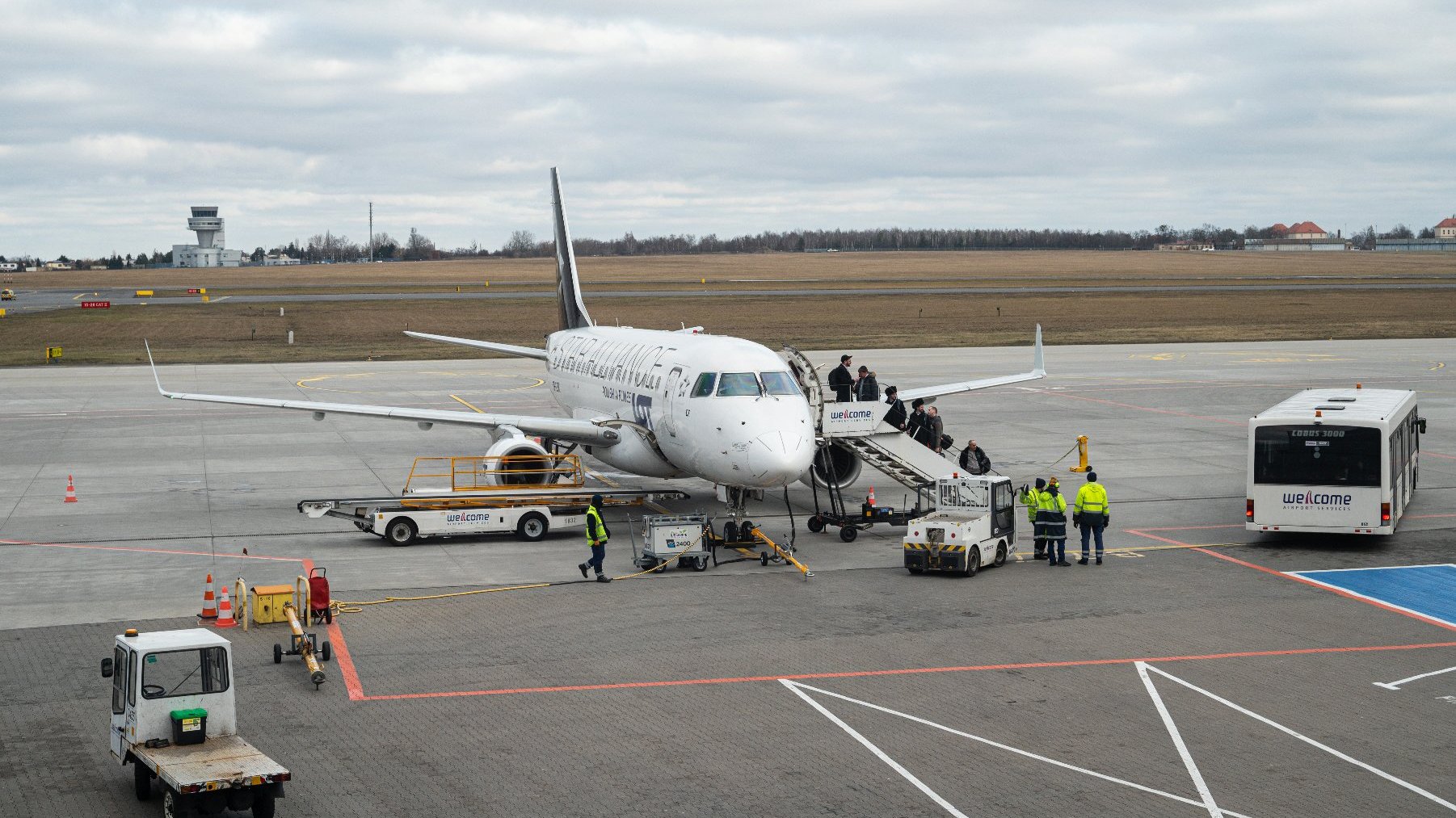 Samolot stojący na pasie, do którego wsiadają pasażerowie - grafika artykułu