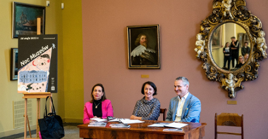 Na zdjęciu, w sali z obrazami monarchów, za stołem siedzą dwie kobiety i mężczyzna