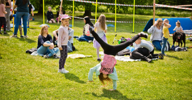 Na zdjęciu dzieci bawiące się na trawie, na pierwszym planie dziewczynka robi gwiazdę