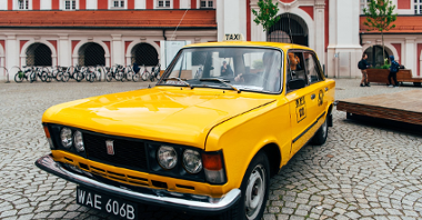 Na zdjęciu żółta starodawna taksówka na dziedzińcu urzędu miasta