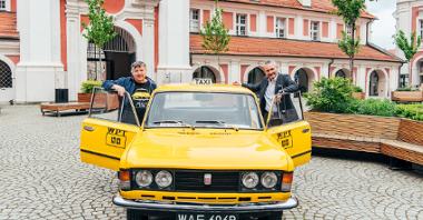Na zdjęciu dwaj mężczyźni stojący przy żółtej taksówce