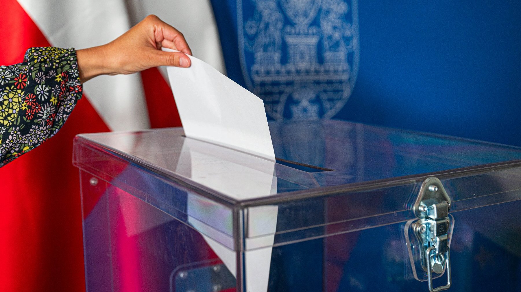 Grafika artykułu: na zdjęciu dłoń wrzucająca kartę do urny wyborczej.