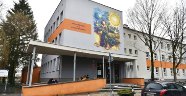 Zdjęcie przedstawia budynek szkoły. Widać na nim także uczniów oraz znajdujący się na budynku mural z podobizną MIkołaja Kopernika.