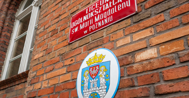 Na zdjęciu ceglana ściana, na niej herb Miasta i tabliczka z nazwą szkoły