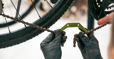 Na zdjęciu dwie dłonie w ciemnych rękawiczkach naprawiające łańcuch roweru