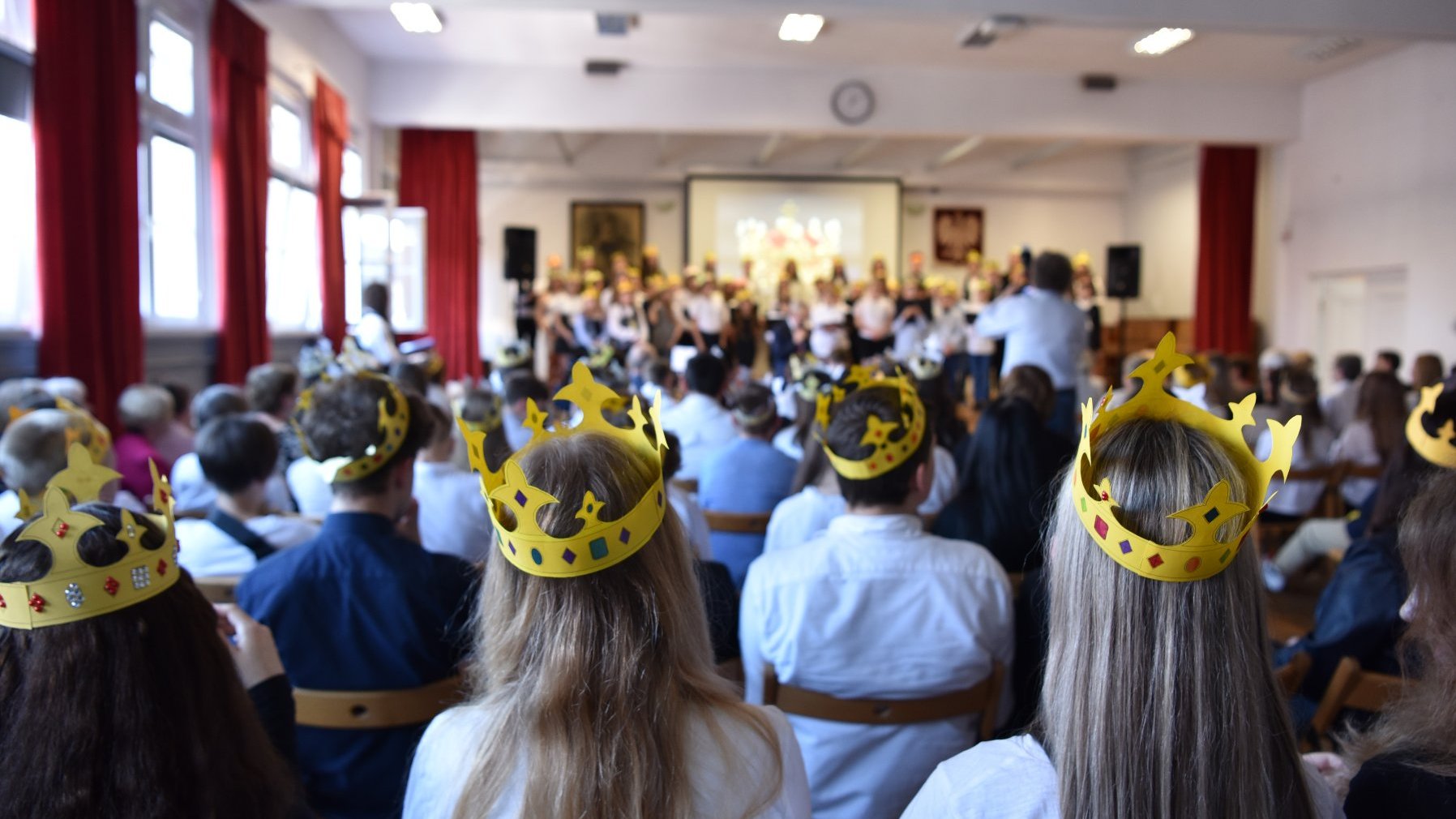 Zdjęcie przedstawia siedzących na sali uczniów w papierowych koronach na głowie.