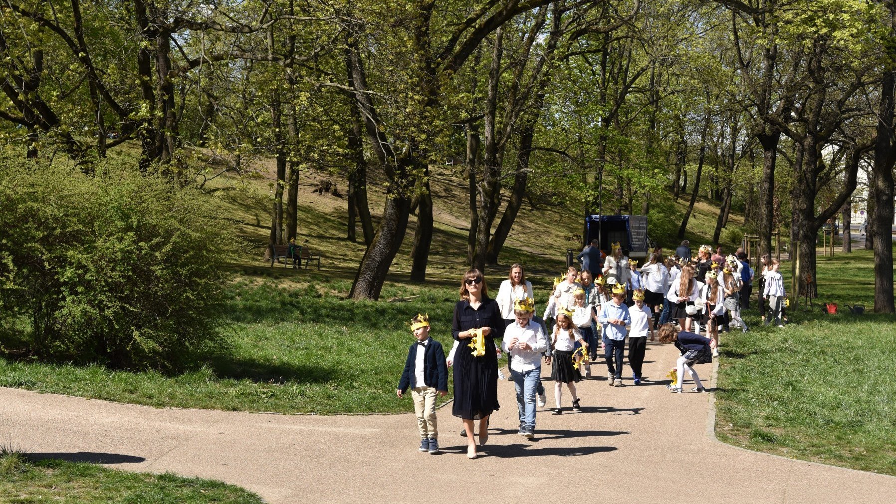 Zdjęcie przedstawia grupę dzieci i nauczycieli idących przez park.