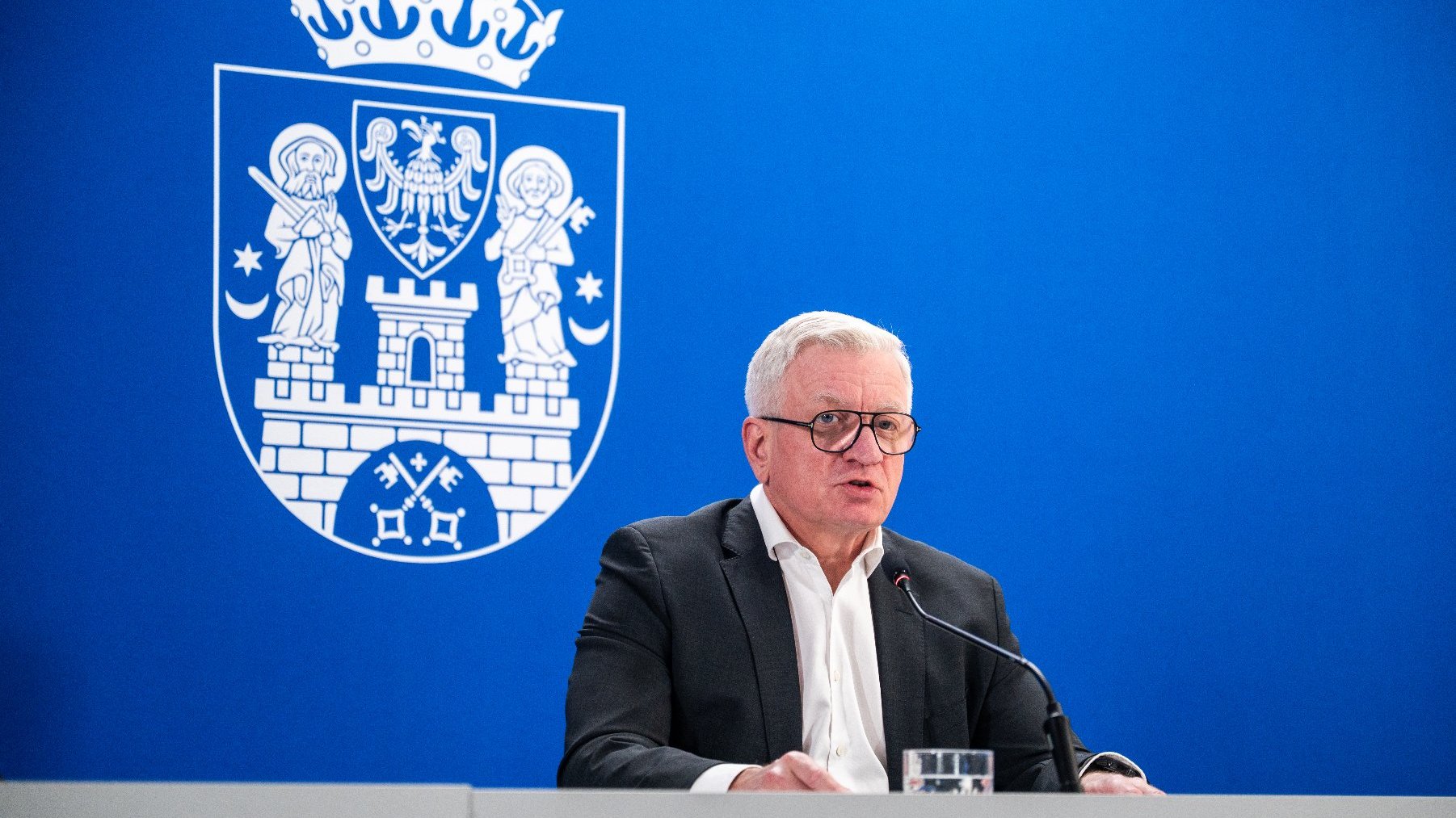 Na zdjęciu prezydent Poznania za stołem konferencyjnym, w tle herb miasta