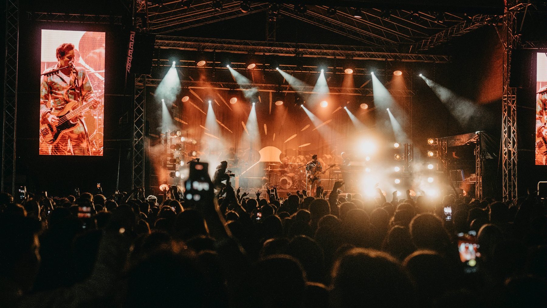 Zdjęcie przedstawia muzyków na scenie oraz tłum ludzi przed sceną. Jednego z muzyków widac też na telebimie.