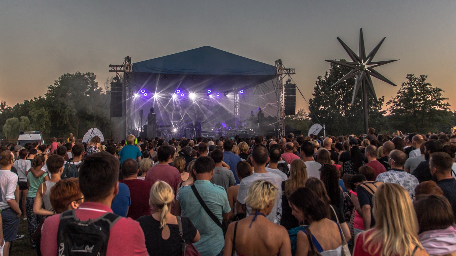 Na zdjęciu scena w plenerze, przed nią tłum ludzi, na scenie widać jasne światła i muzyków