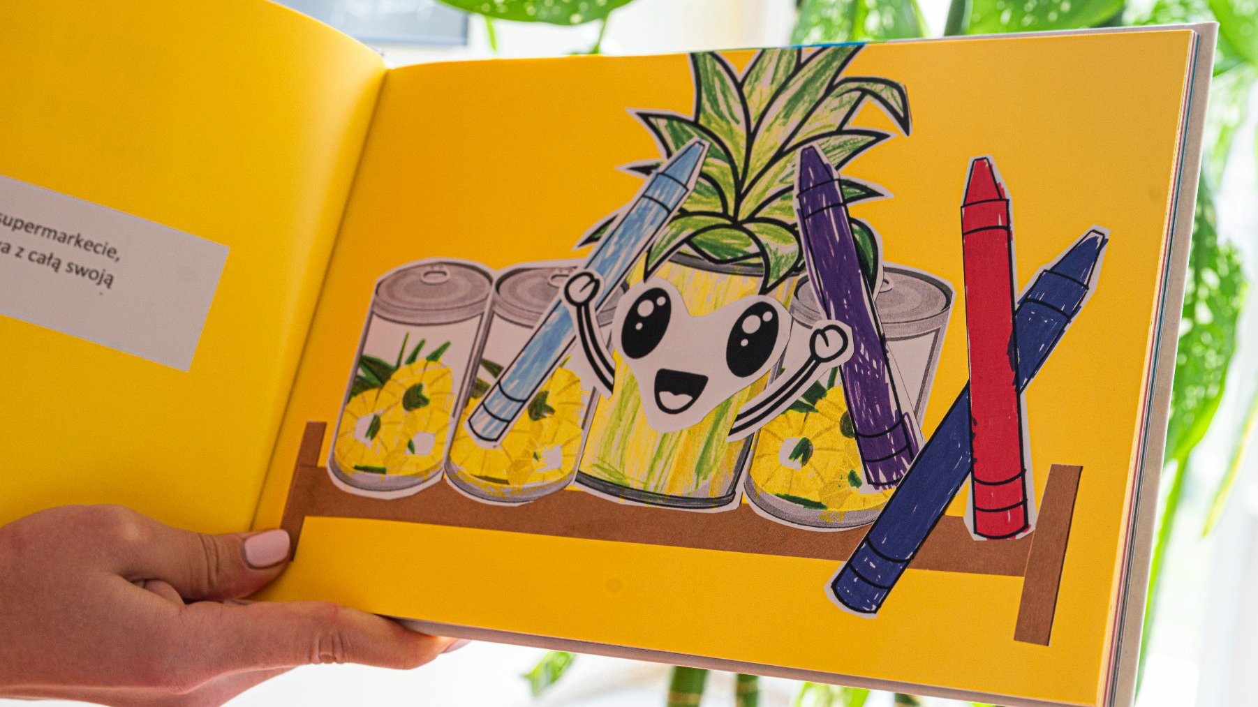 Na zdjęciu wnętrze książeczki - na żółtym tle narysowane są puszki ananasa oraz kredki