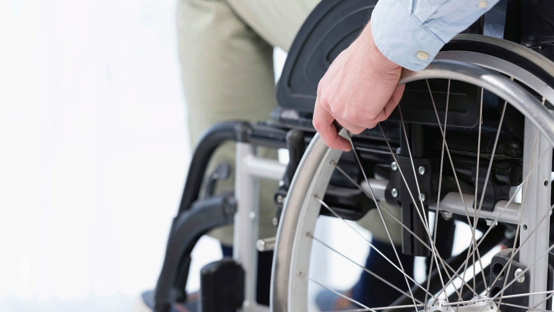 Na zdjęciu osoba na wózku inwalidzkim, widać tylko dłoń i koła wózka