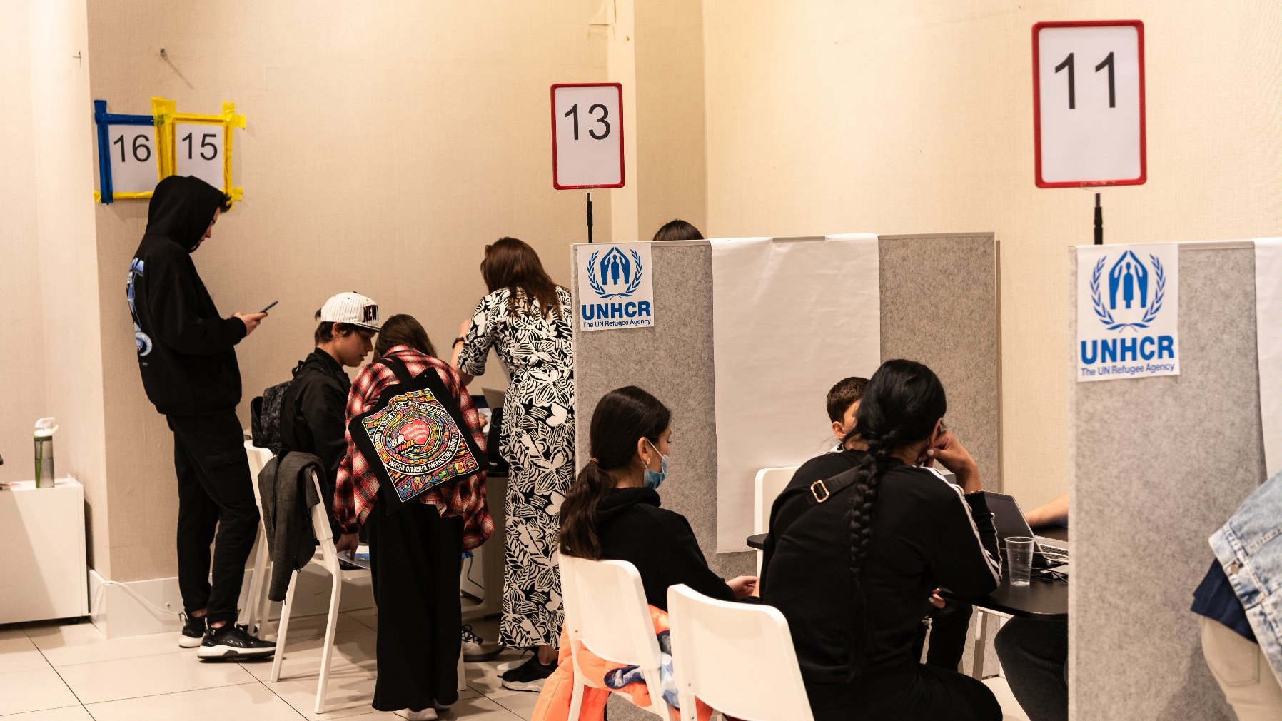 Na zdjęciu stoiska w Centrum UNHCR, przy nich ludzie, siedzący tyłem do obiektywu