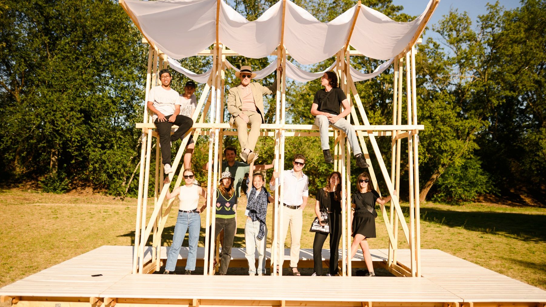 Na zdjęciu grupa ludzi stojąca w drewnianej, zadaszonej konstrukcji w lesie