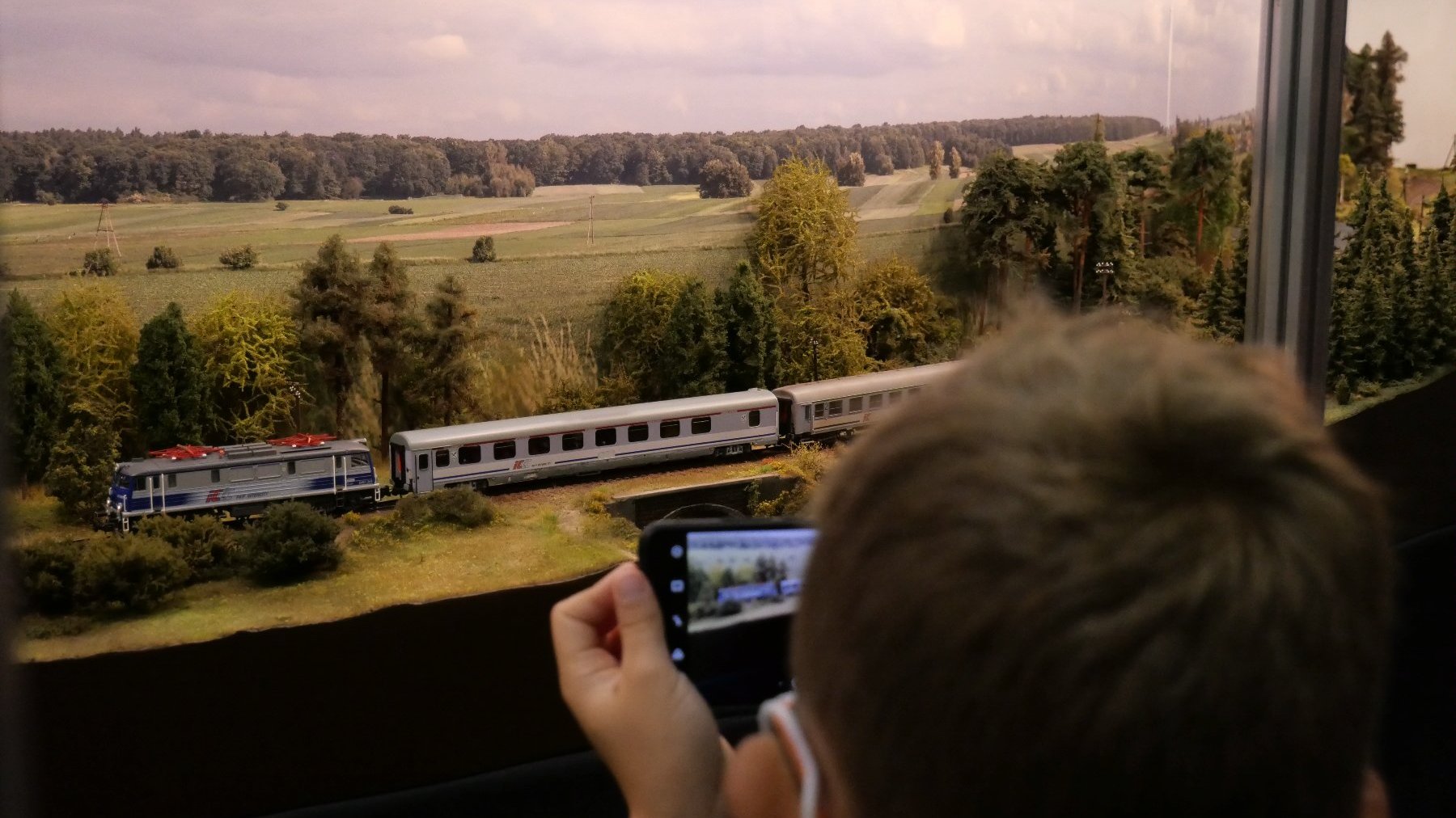 Zdjęcie przedstawia chłopca przed modelem pociągu.