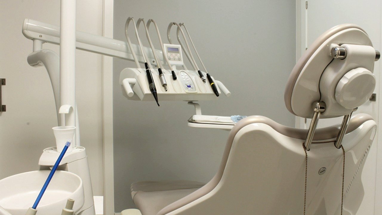 Wnętrze gabinetu stomatologicznego. Na pierwszym planie fotel stojący tyłem, za nim panel z narzędziami dentystycznymi - grafika artykułu