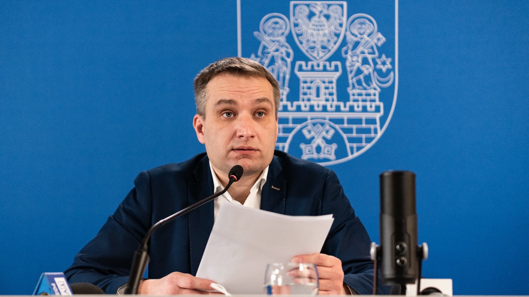 Na zdjęciu Mariusz Wiśniewski, zastępca prezydenta Poznania przy mikrofonie, za nim granatowa ścianka z herbem Miasta