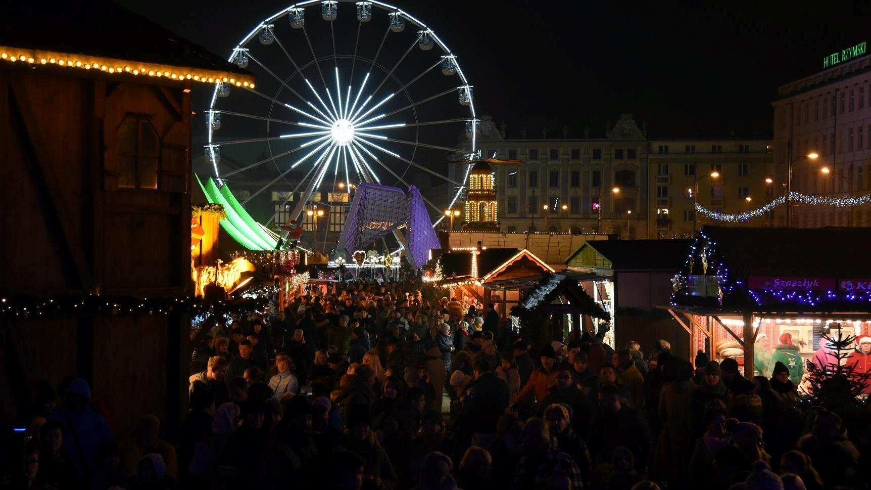 Zdjęcie przedstawia Betlejem Poznańskie na placu Wolności. Widać na nim młyńskie koło, drewniane domki oraz tłum ludzi. - grafika artykułu
