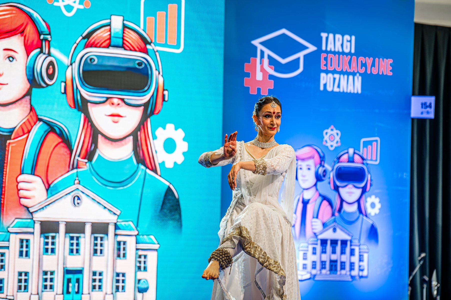 Zdjęcie przedstawia młodą osobę stojącą na przeciwko człowieka przebranego za Leszego. W tle widać stoiska z książkami i ludzi.