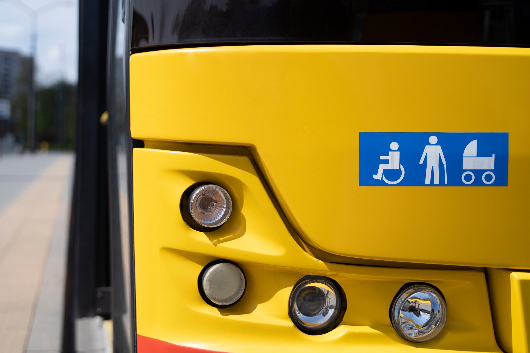 Zdjęcie przedstawia osobę na wózku wjeżdżająca po specjalnej platformie podjazdowej do autobusu.