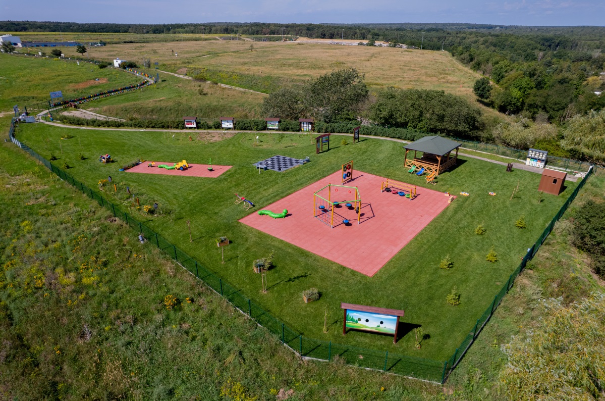 Zdjęcie przedstawia plac zabaw. Znajdują się na nim elementy wykonane na przykład z drewna czy pomalowanych opon.