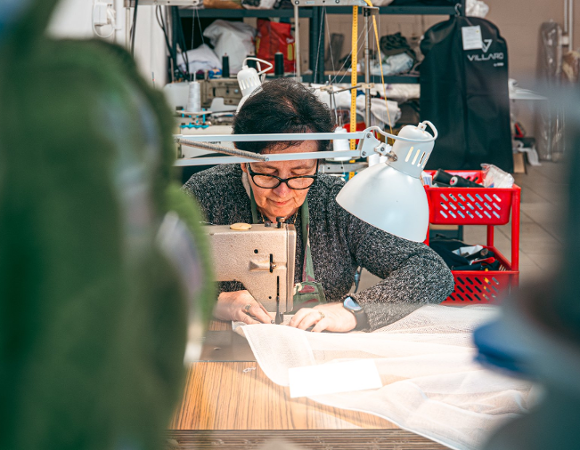 Zdjęcie przedstawia pracującą na maszynie do szycia w zakładzie krawieckim.