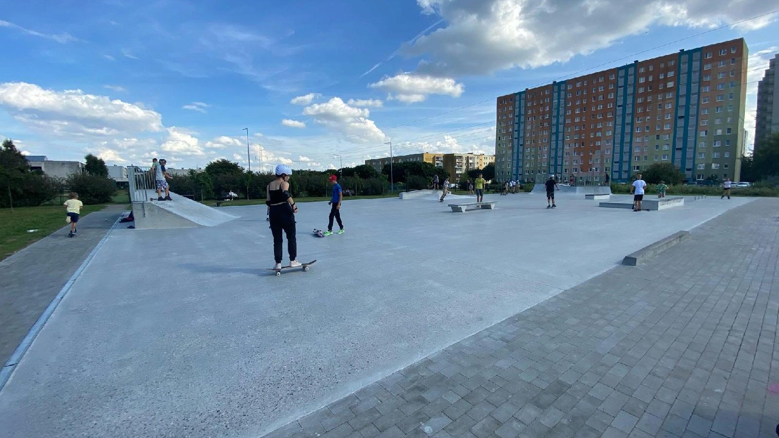 Zdjęcie przedstawia skatepark. Widać na nim młode osoby jeżdżące na deskorolkach, w tle znajdują się bloki - grafika artykułu