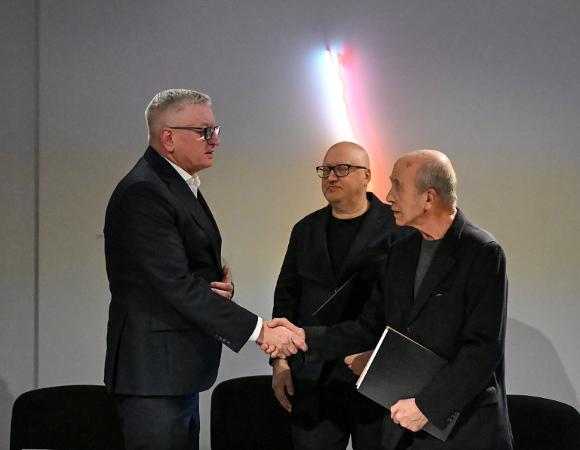 Zdjęcie przedstawia trzech mężczyzn. Dwóch podaje sobie ręke.