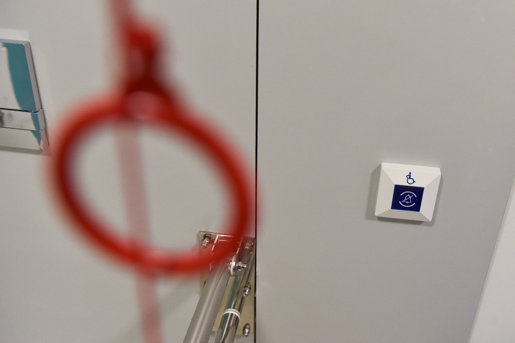 Zdjęcie przedstawia zbliżenie na ścianę w obiekcie użyteczności publicznej, wyposażoną w udogodnienia dla osób z niepełnosprawnościami.