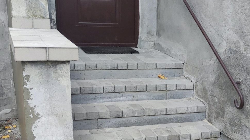 Zdjęcie przedstawia szare schody z poręczą.