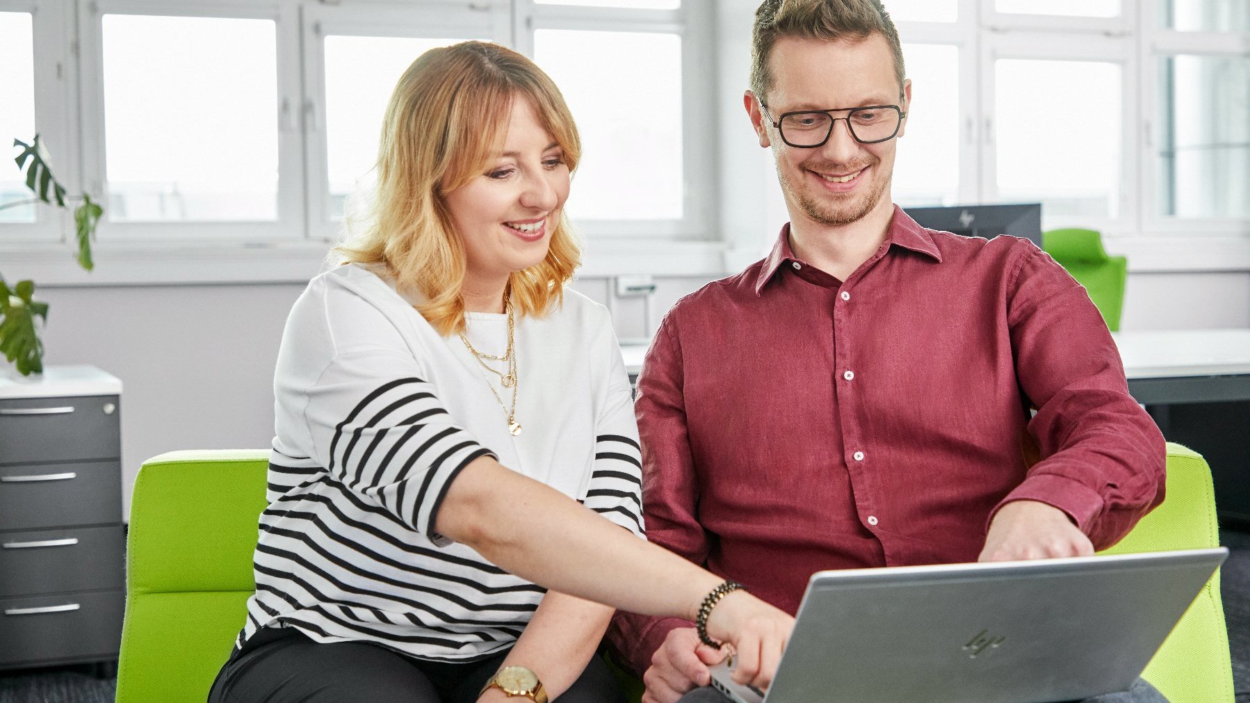 The photo shows two people inside the office. They are smiling, watching something on a laptop together.