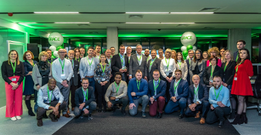 The photo shows a group of male and female employees, people attending the official opening of Grace's office in a group photo. In the centre are the company's officers and the Mayor of Poznań, Jacek Jaskowiak. In the background you can see green and white balloons with the Grace company logo.