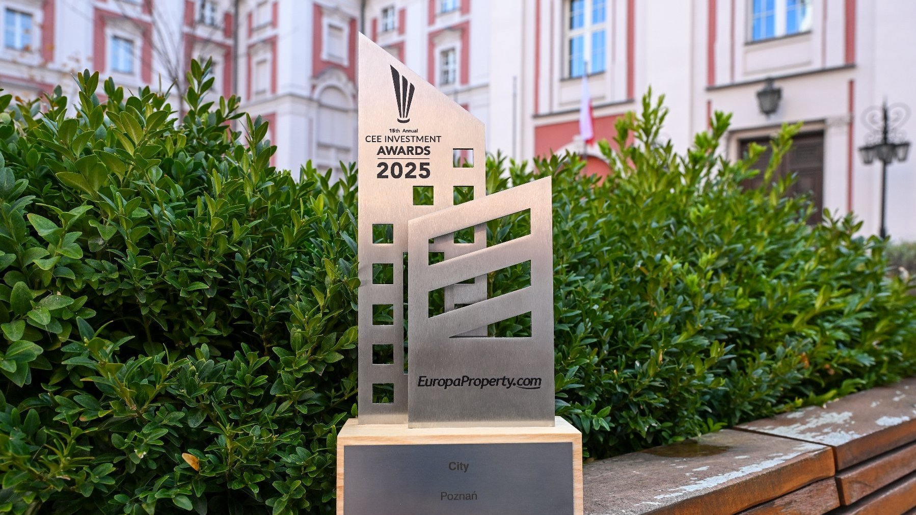 A metal award depicting two intersecting skyscrapers. In the background, vegetation and the City Hall building.