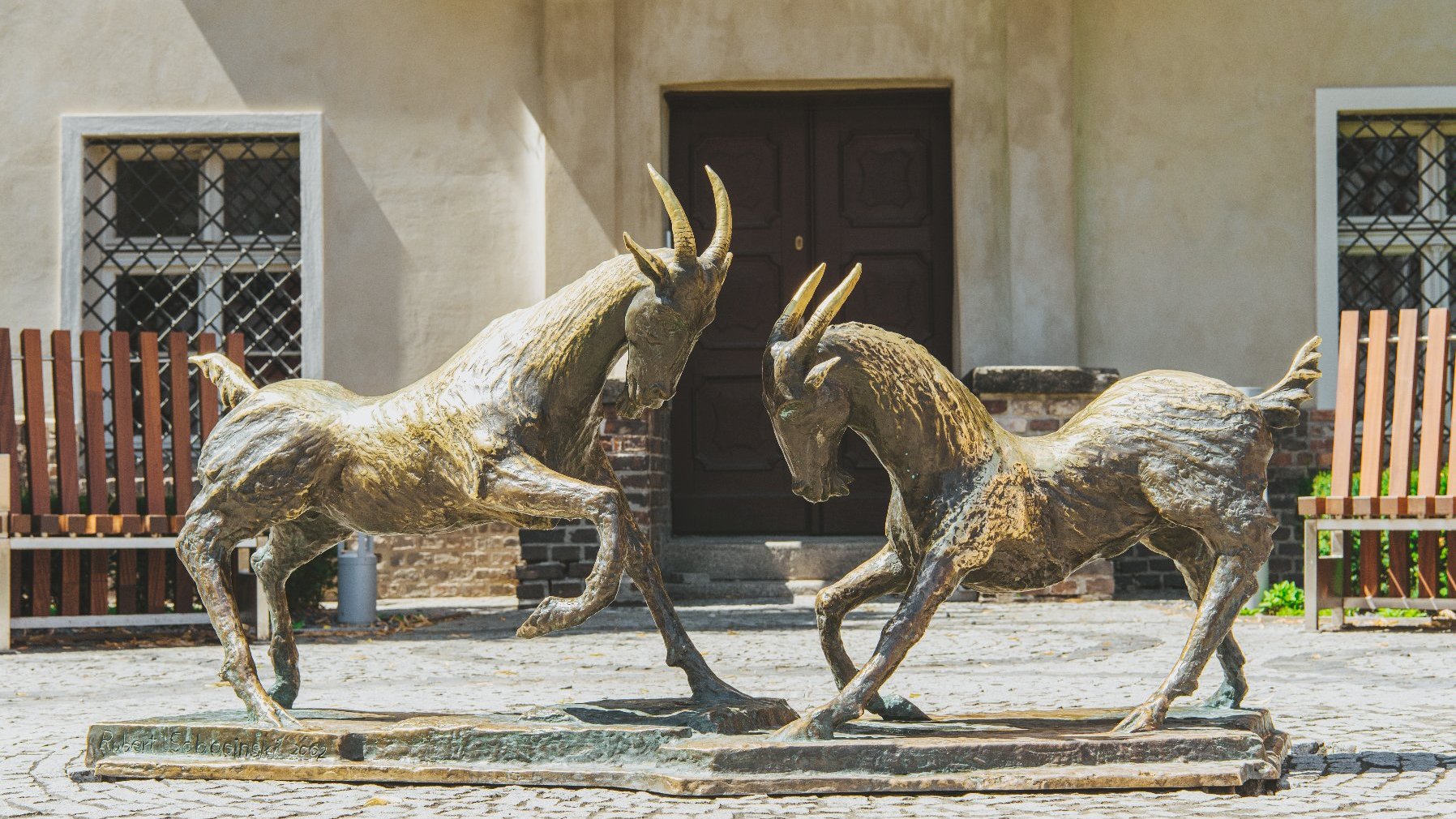 a sculpture of the Poznań Goats figthing. the sculpture is in front of a building