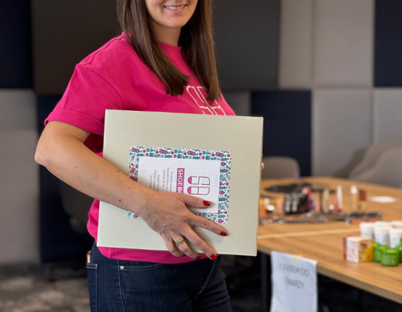 Kobieta w różowej koszulce trzyma w ręce pudełko po butach podpisane "Shoebox".