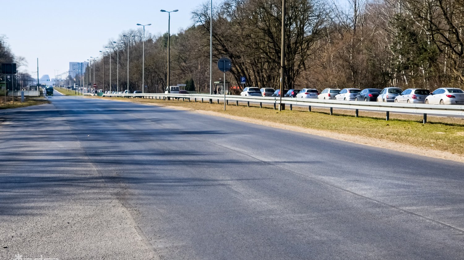 Równa asfaltowa nawierzchnia ul. Warszawskiej po remoncie, po bokach zieleń, na prawym poboczu zaparkwoane samochody osobowe
