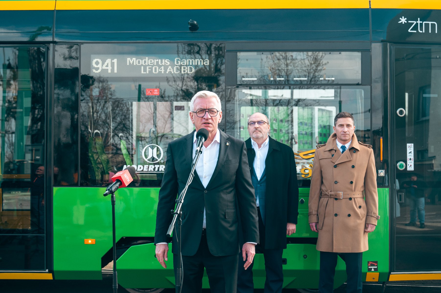 Prezydent Poznania mówiący coś do mikrofonu, w tle dwóch mężczyzn, za nimi nowy tramwaj - grafika artykułu