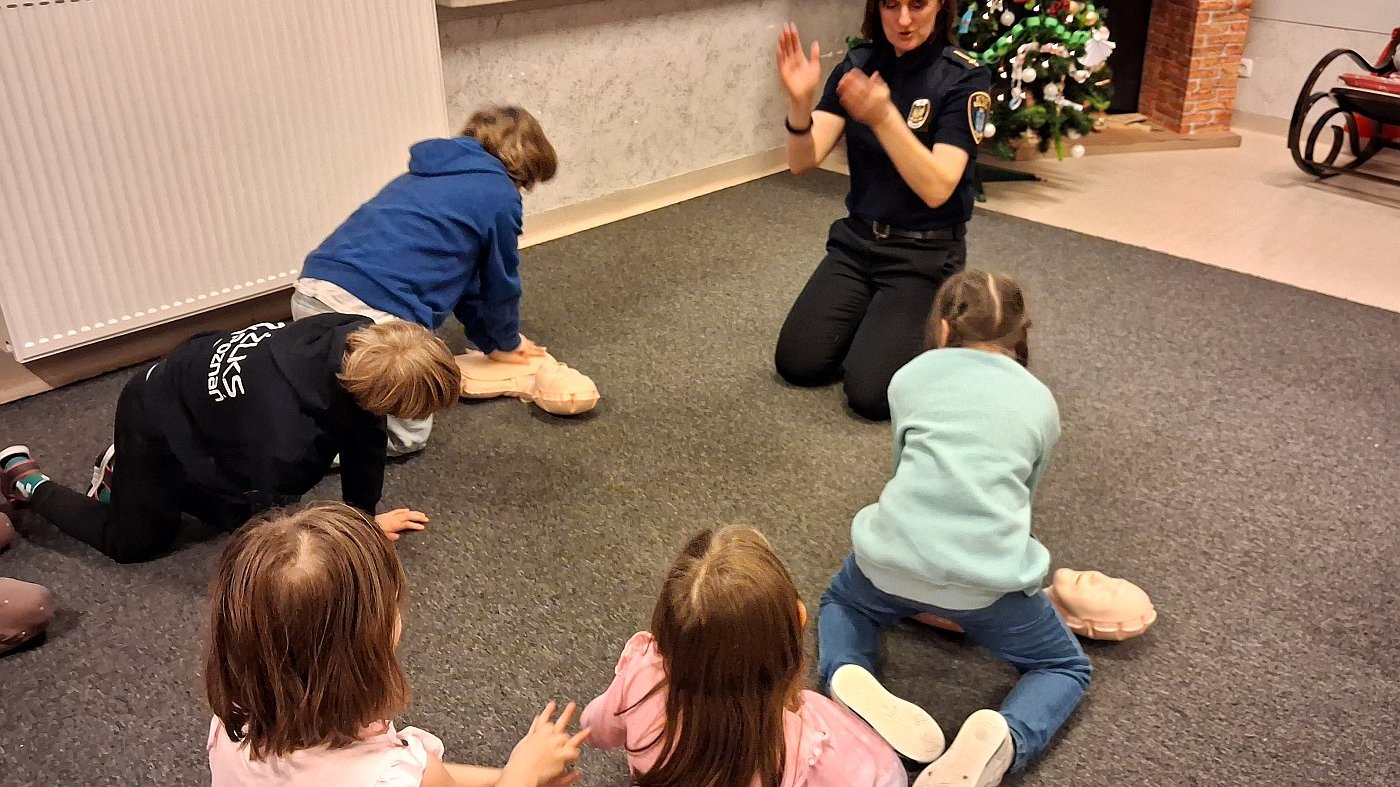 strażniczka instruuje ćwiczące na mini fantomach dzieci o rytmie uciśnięć