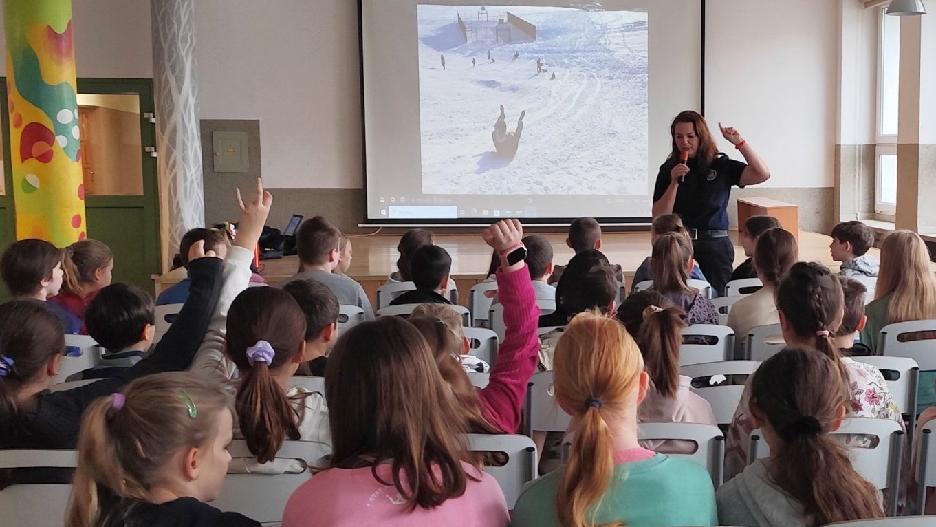 strażniczka omawia z uczniami zasady bezpieczeństwa podczas zjeżdżania na sankach zilustrowane prezentacją na ekranie